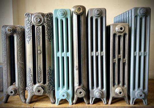 A variety of ornate cast iron radiators in different finishes lined up against a wall.