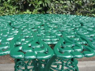 Freshly restored ornate green cast iron garden table with detailed lattice design.